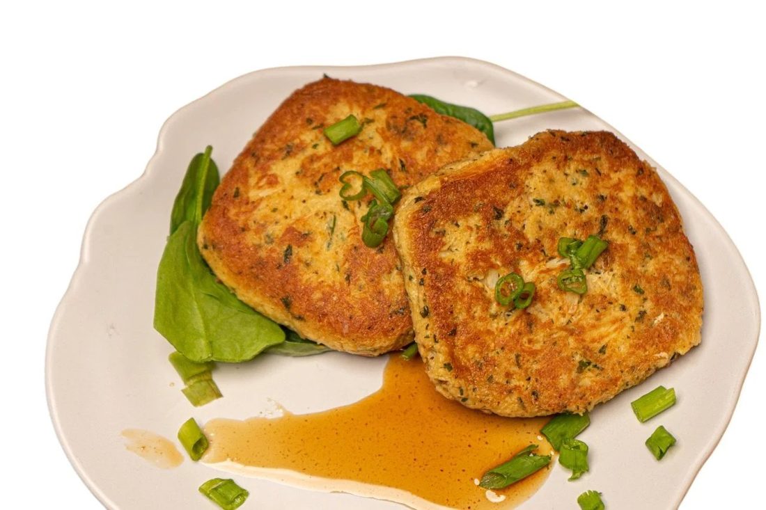 Two golden-brown BB's homemade crab cakes plated with greens and sauce